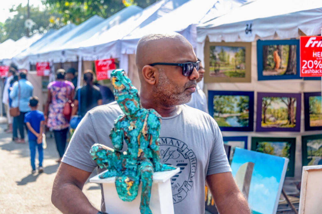 A bustling street scene featuring people browsing and vendors showcasing various art pieces for sale.