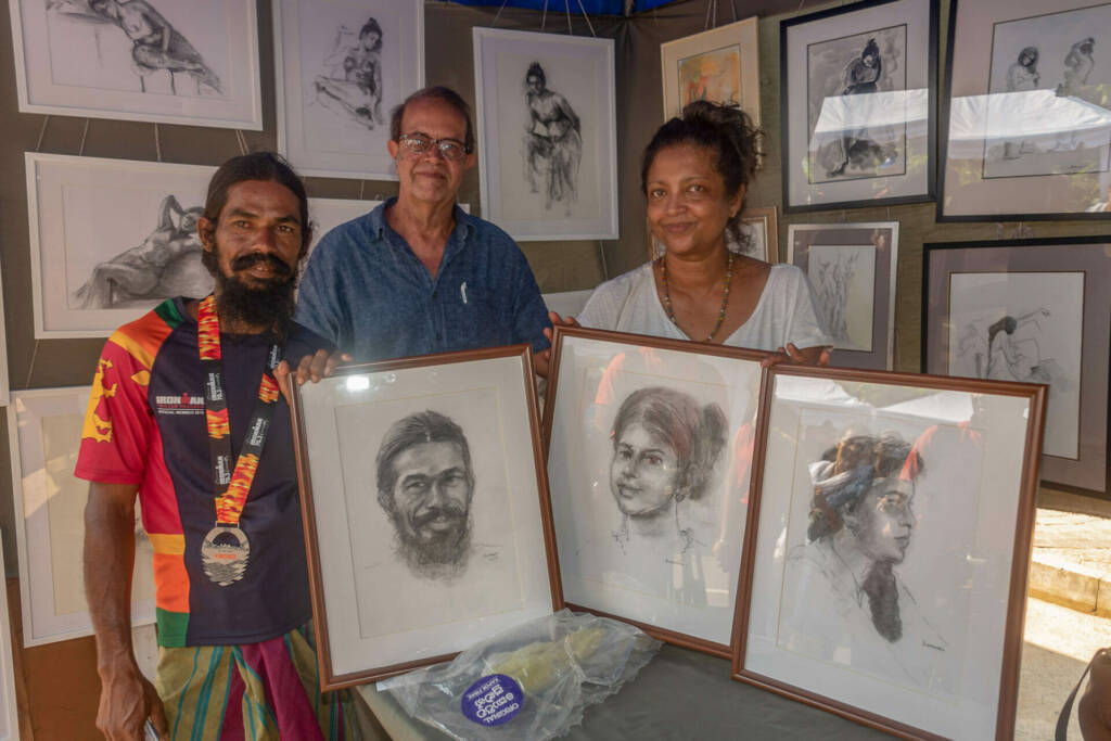 Two individuals proudly display framed drawings in front of a table, showcasing their artistic creations.