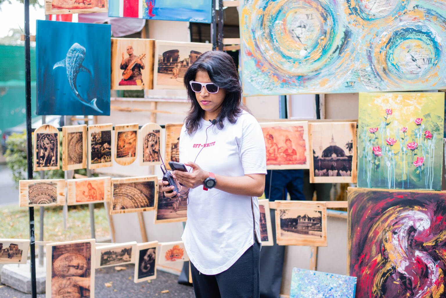 A woman poses in front of a table adorned with an array of vibrant paintings.