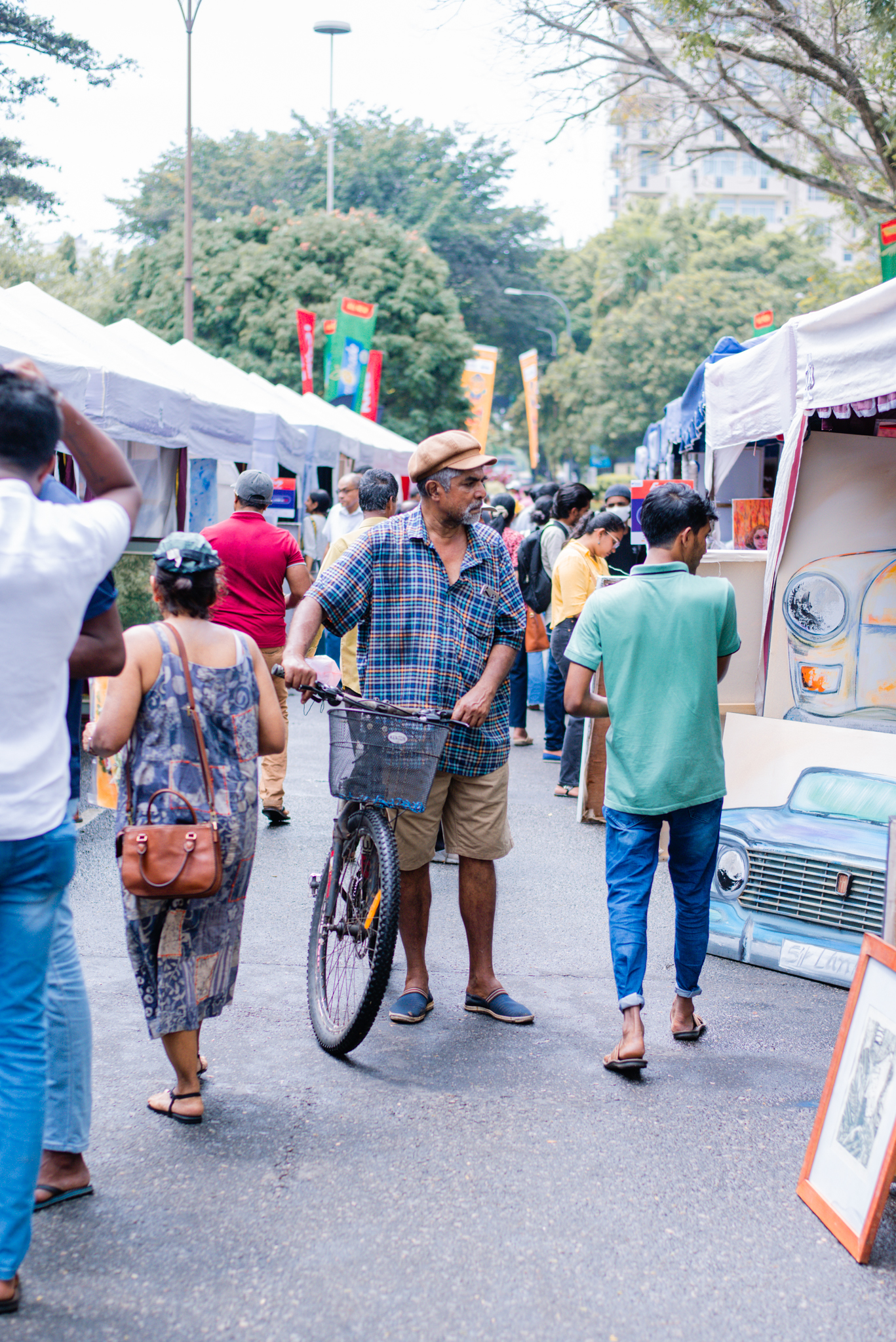 People stroll down the street, while a man with a bicycle stops to looking at the painting showcase.