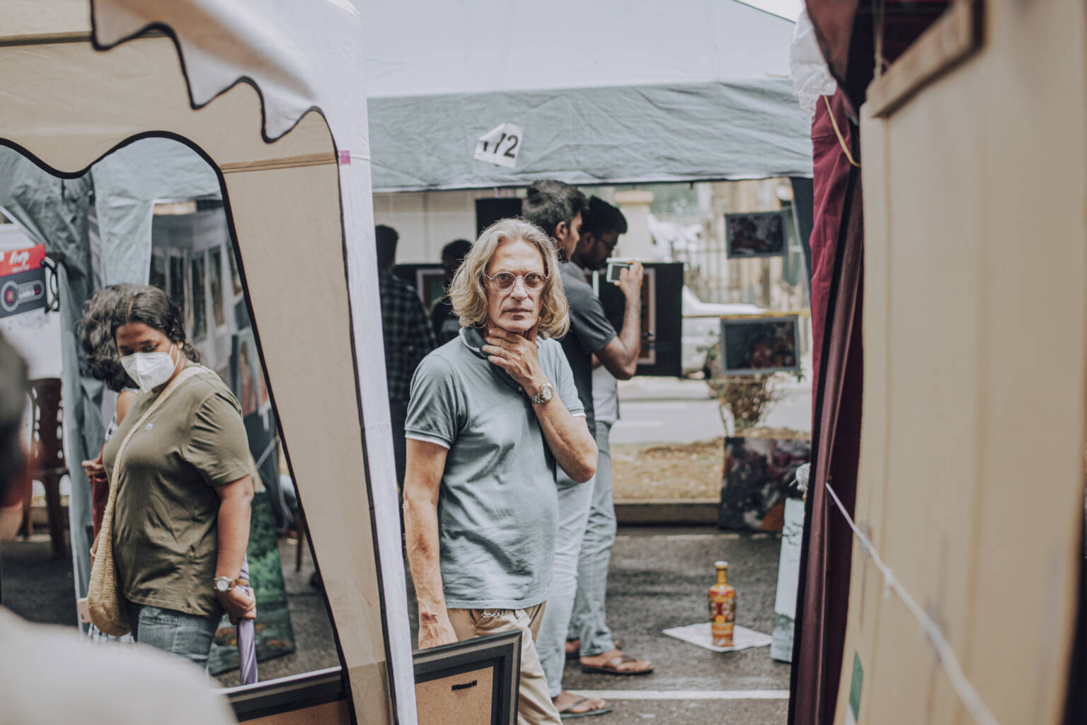 A man poses for a photo shoot while standing under a tent, showcasing a relaxed and confident demeanor.